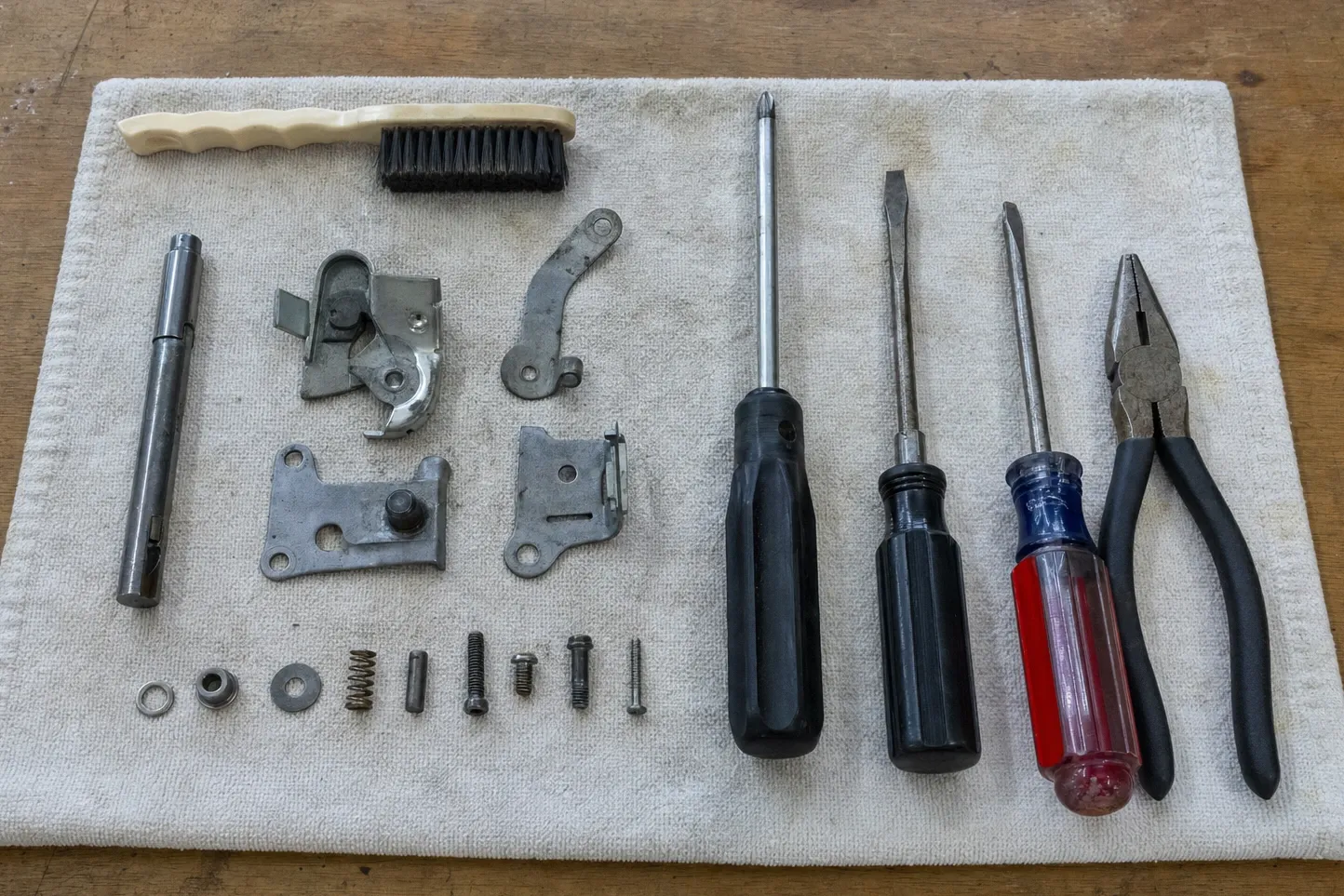 Oven door latch assembly, hinge arm and two mounting plates laid out with a spring, screws and hand tools