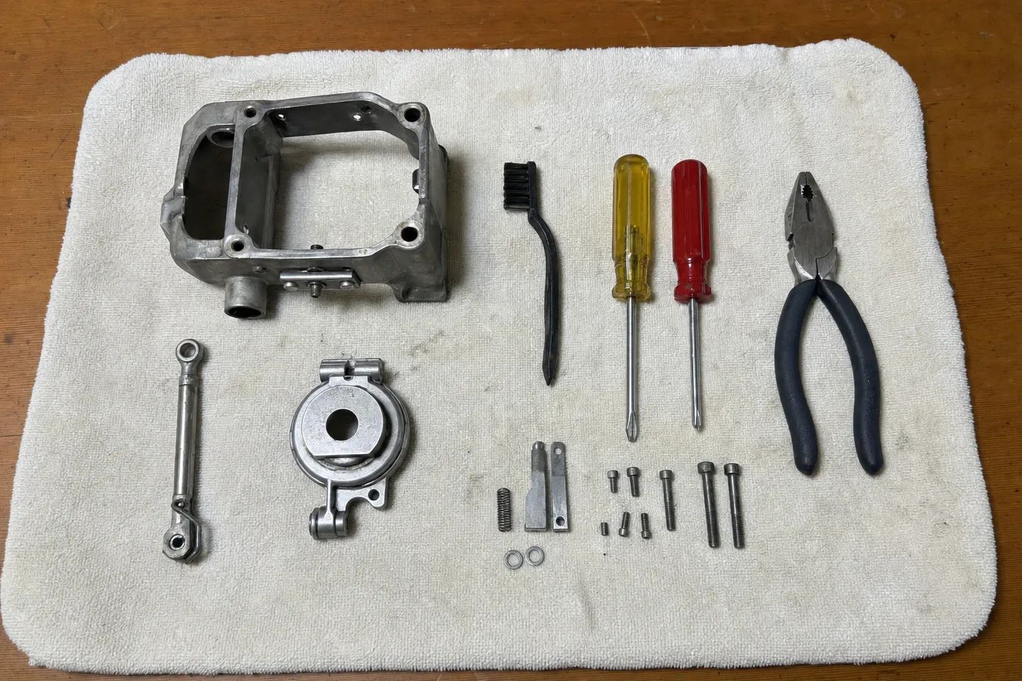 Cast aluminium housing, linkage rod and a flanged bearing housing laid out on a towel beside screwdrivers, pliers and fixings